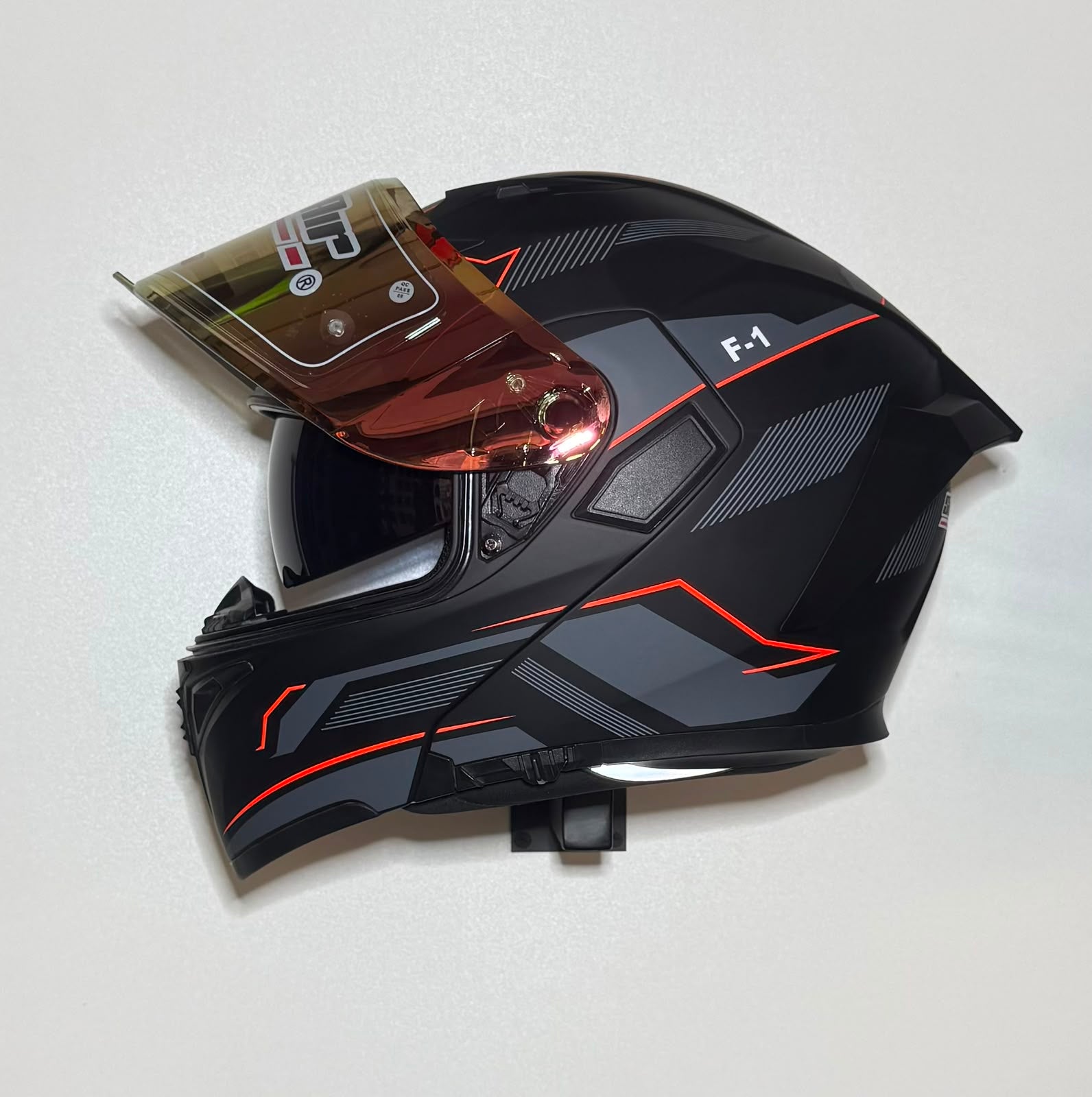 Super Air F-1 helmet side view with visor open showing gold iridium visor and F-1 badging on matte black shell